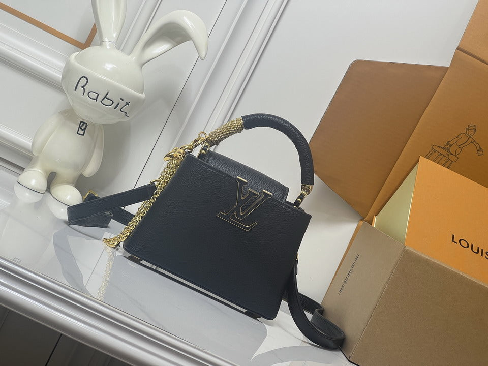Structured black pebbled leather mini handbag with gold-tone monogram closure, braided chain accent, top handle, and shoulder strap