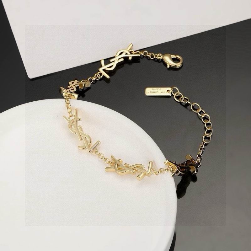 Gold-tone monogram charm chain bracelet with lobster clasp, displayed on a white surface